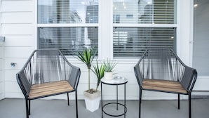 Zwei schwarze Korbstühle mit Holzsitzen und ein kleiner weißer Tisch mit einem Blumentopf dazwischen.