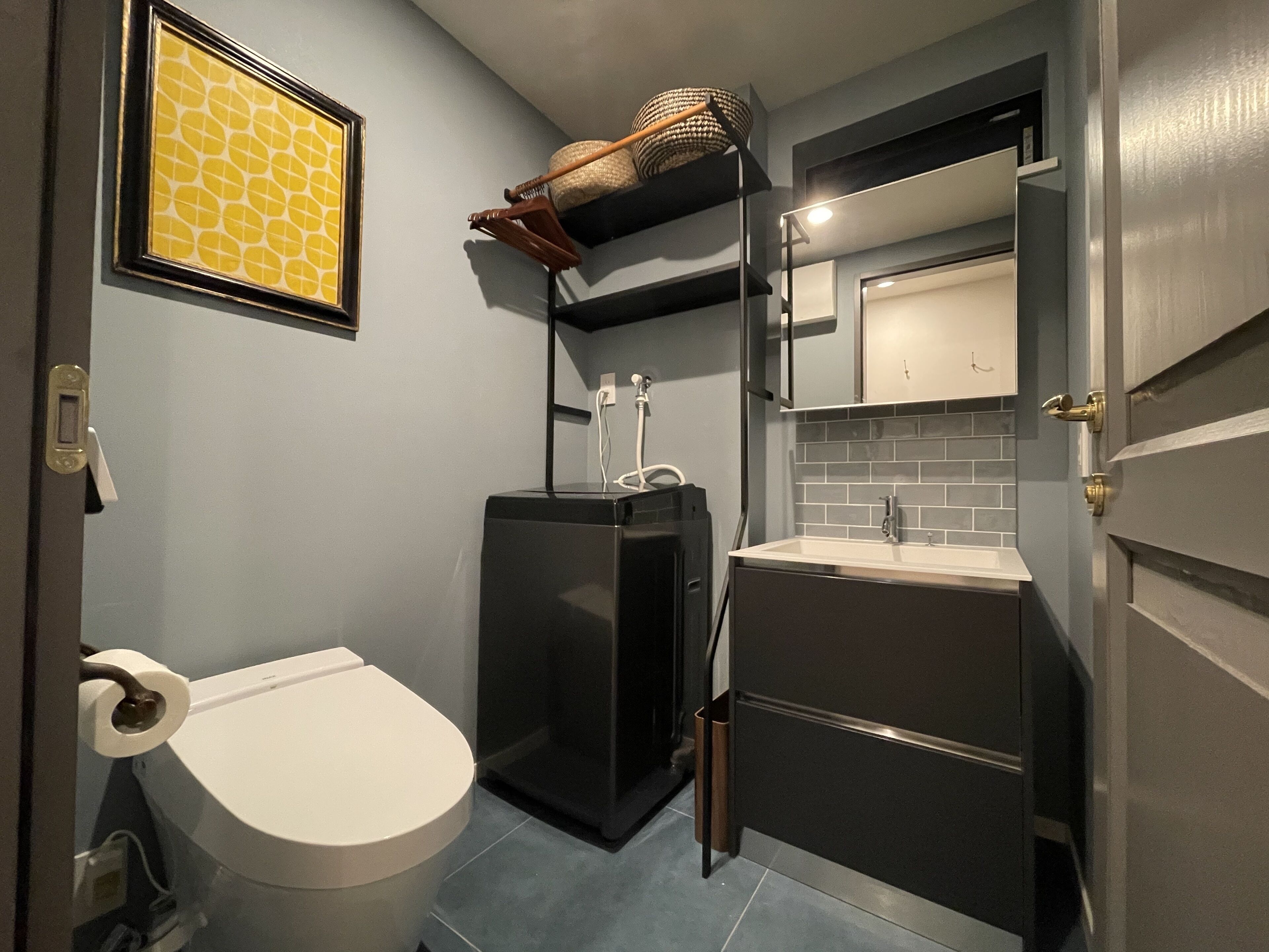 Et lille badeværelse med toilet, et sort væghængt håndvask og et spejl over vasken.