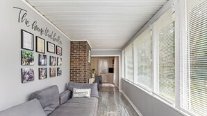 A hallway with a grey sofa, framed photos on the wall, and a brick accent wall. - Pet Friendly Quiet Retreat Near Nashville (Kingston Springs)