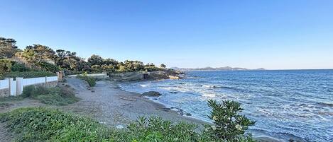 Una carretera costanera amb una platja rocosa, una tanca blanca i vegetació.