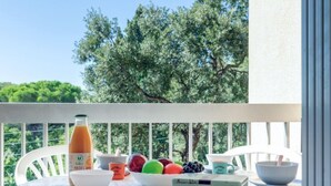A balcony with a table set for breakfast, featuring a bottle of juice, bowls, a fruit bowl, and a box of biscuits. - La Chênaie by Interhome (Saint Aygulf)