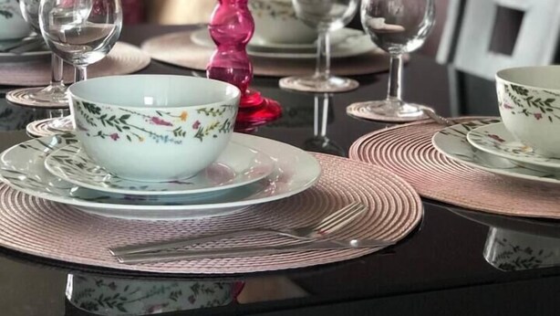 Ein Esstisch gedeckt mit Schalen, Tellern und einer rosa Kerze mit floralem Muster.