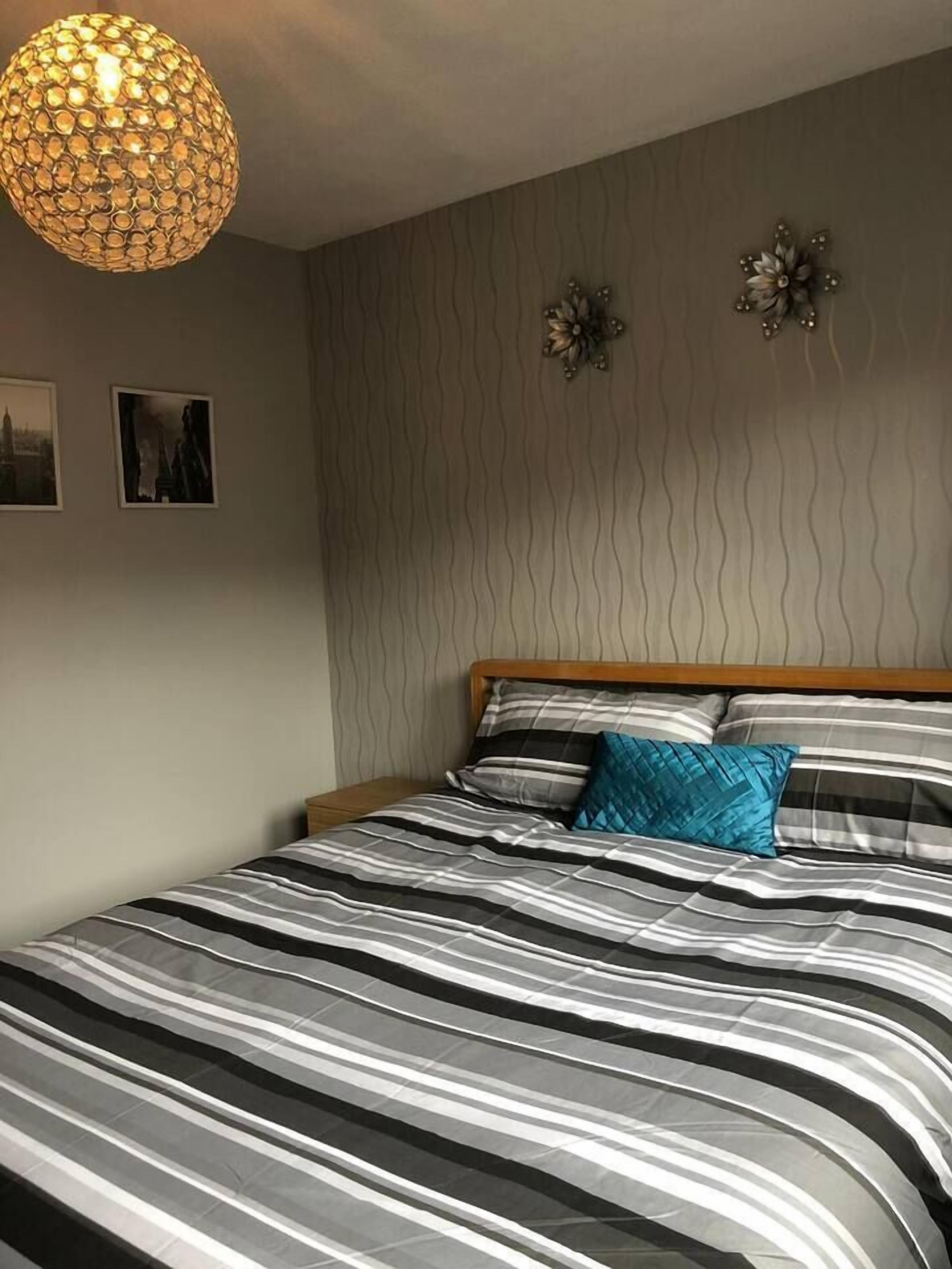 A neatly made bed with striped bedding, a patterned wall, and a decorative light fixture.
