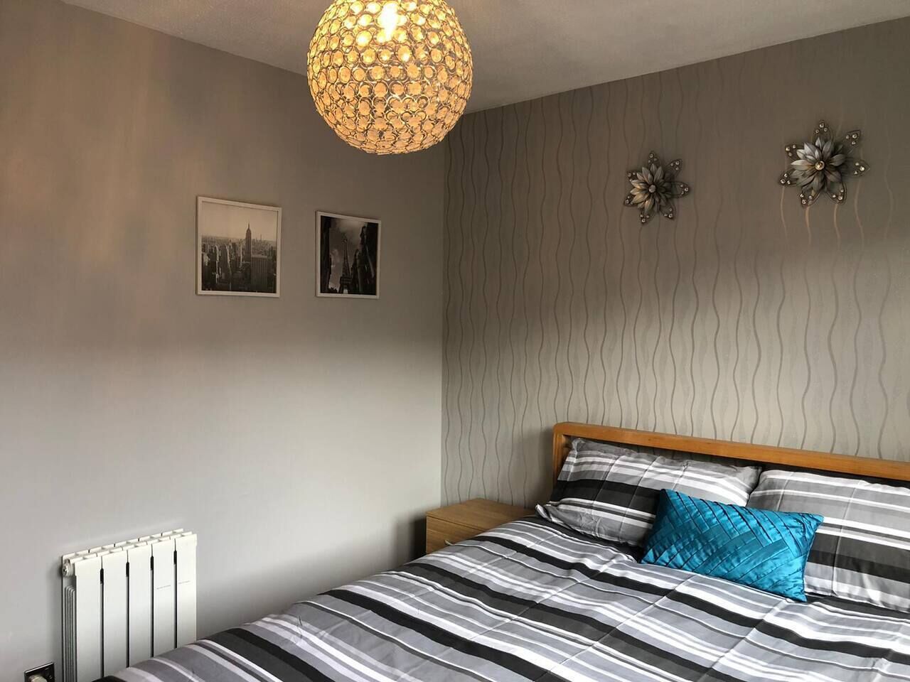 A bedroom with a bed, a radiator, two wall-mounted pictures, and a textured wall.