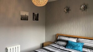Ein Schlafzimmer mit einem Bett, einem Heizkörper, zwei Wandbildern und einer strukturierten Wand.