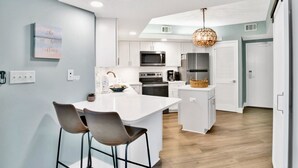 Cozinha moderna com armários brancos, uma ilha central e um lustre pendente.