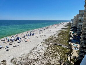 A beach with umbrellas and people, a boardwalk, and a hotel building with balconies. - Summer House 1003B | Direct Beach Front, Spacious, Oversized Beach Deck! (Orange Beach)