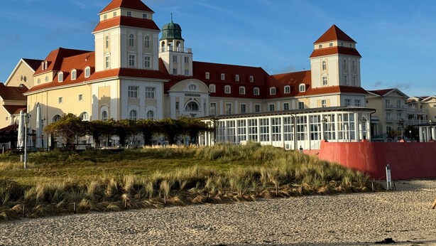 Ein großes, historisches Gebäude mit mehreren Türmen und einer zentralen Kuppel, umgeben von einer Schotterfläche und einigen Rasenflächen.