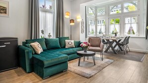 Ein Wohnzimmer mit einem grünen Sofa, einem kleinen runden Tisch und einem Essbereich mit Tisch und Stühlen.