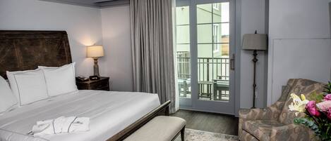 Habitación de hotel con una cama grande, un banco, una silla, una mesita de noche y vistas al exterior a través de una puerta corredera.