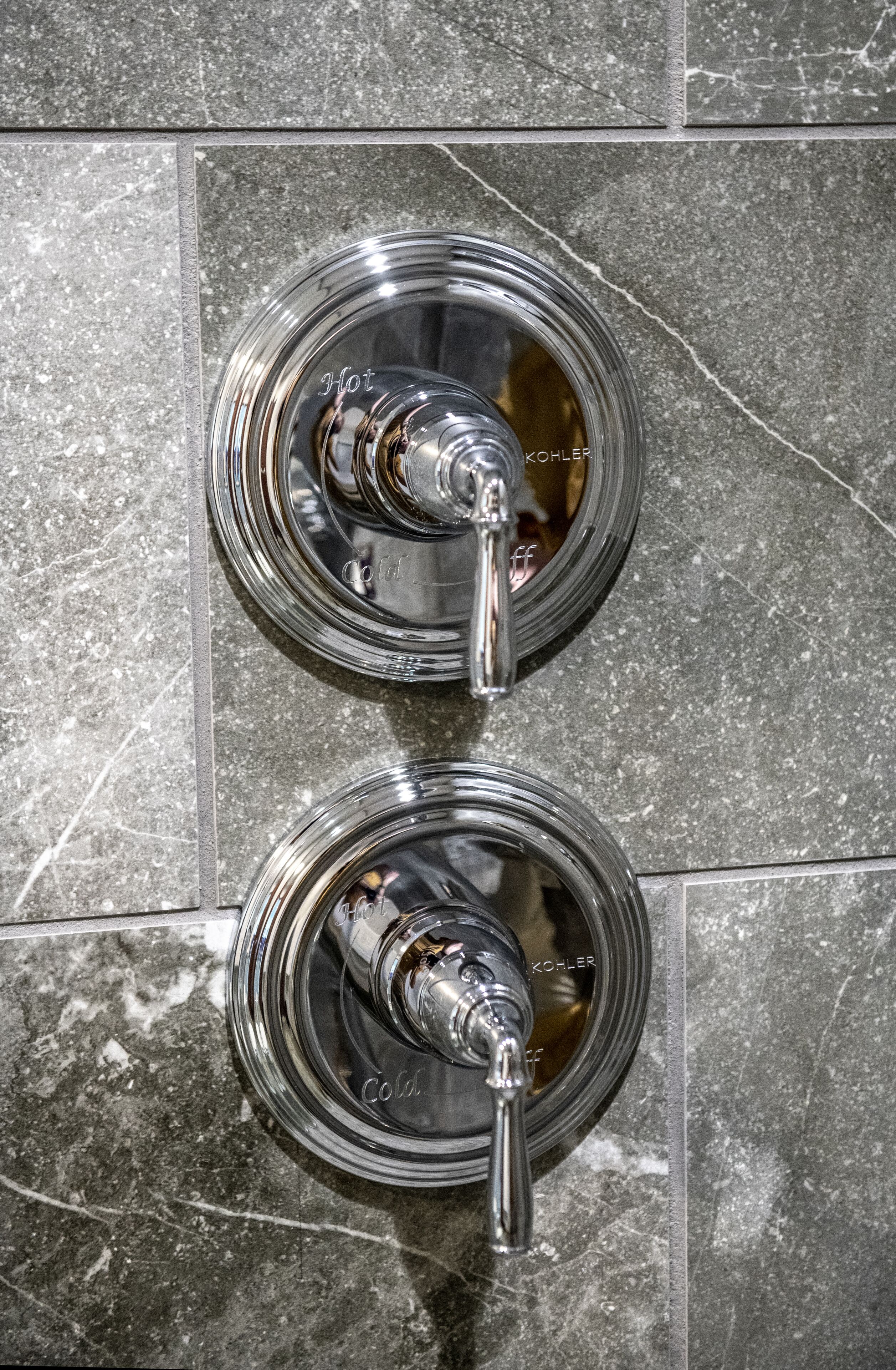 Two chrome-finished faucets with the brand name "Kohler" on a tiled wall.