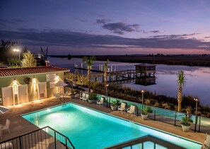 A pool area with a view of a calm body of water, a dock, and a building with a sign warning about the water. - Oaks on the River (Darien)