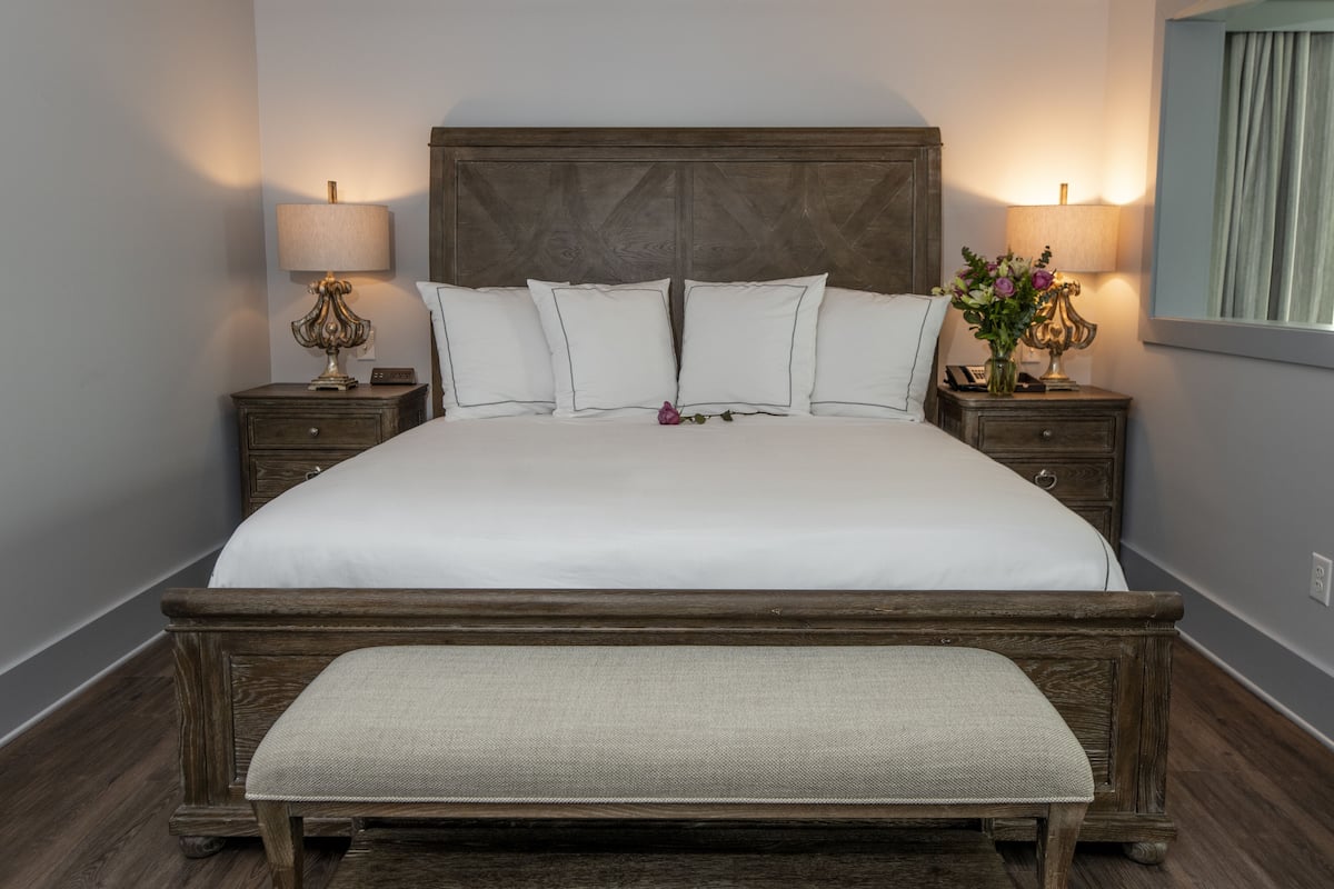 A large bed with a wooden headboard, two bedside tables with lamps, and a bench at the foot of the bed.
