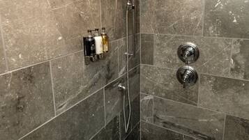 Una ducha con cabezal de ducha de mano, grifo empotrado en la pared y suelo de azulejos.