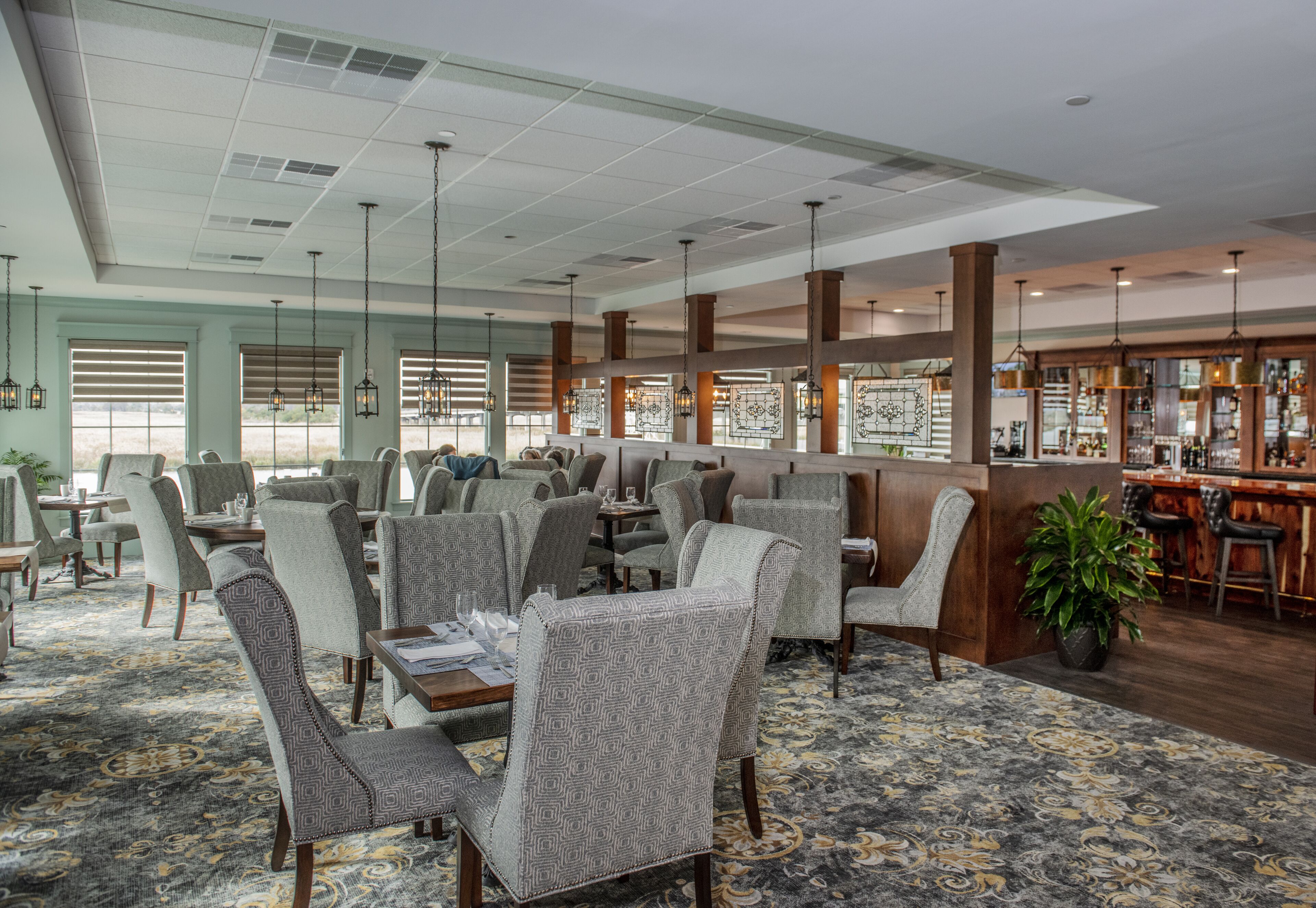 A spacious restaurant with high ceilings, patterned carpet, and a bar area.