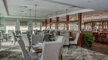 A spacious restaurant with high ceilings, patterned carpet, and a bar area.