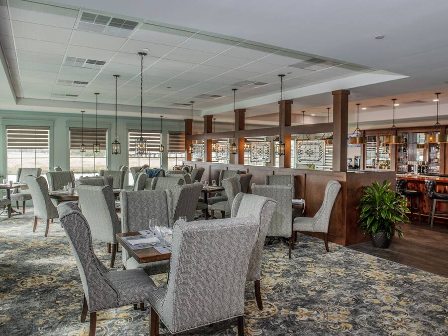 A spacious restaurant with high ceilings, patterned carpet, and a bar area.