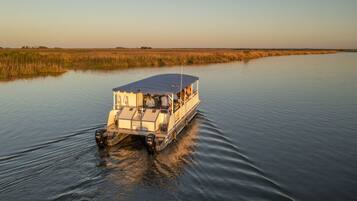 A boat with a covered deck and a cabin, moving through calm water with a flat landscape in the background.
