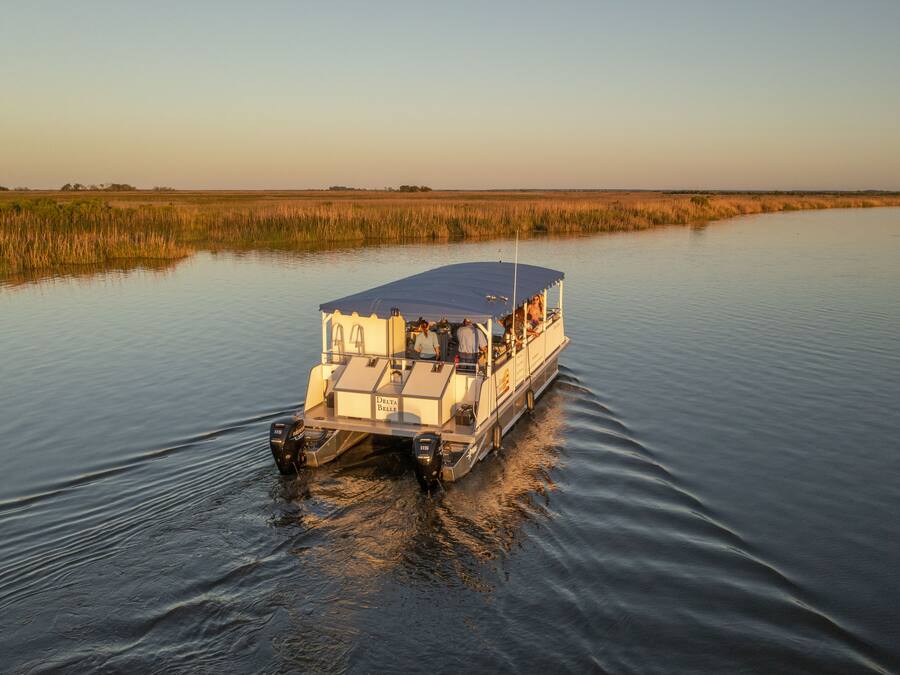 A boat with a covered deck and a cabin, moving through calm water with a flat landscape in the background.