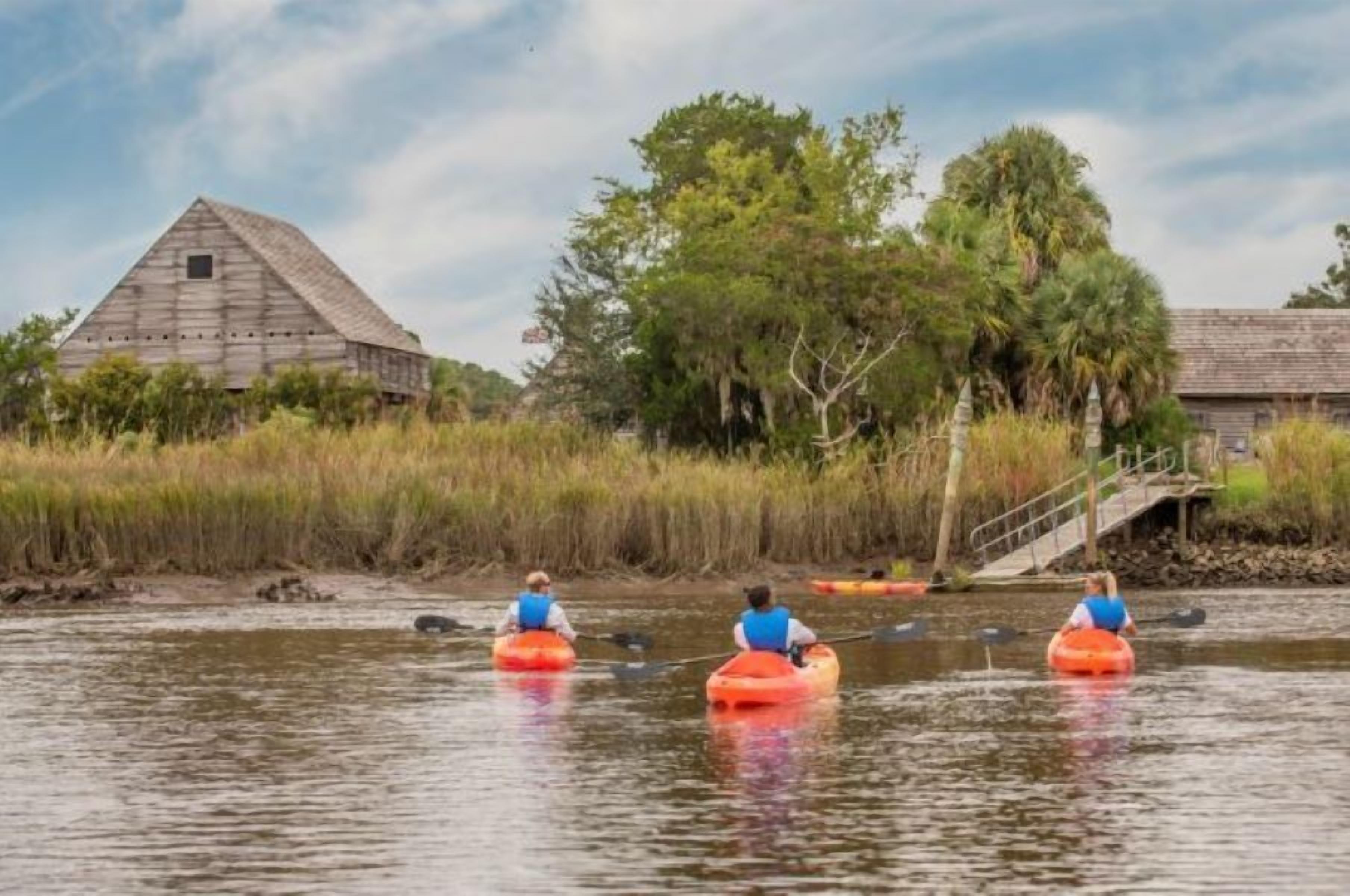 A river with kayakers, a wooden barn, and a bridge.