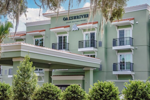 A multi-story building with balconies, a sign reading "OAKS ON RIVER LUXURY BOUTIQUE RESORT," and a logo above the sign. - Oaks on the River (Darien)