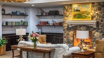 A cozy lobby with a fireplace, bookshelves, a patterned sofa, and a chandelier.