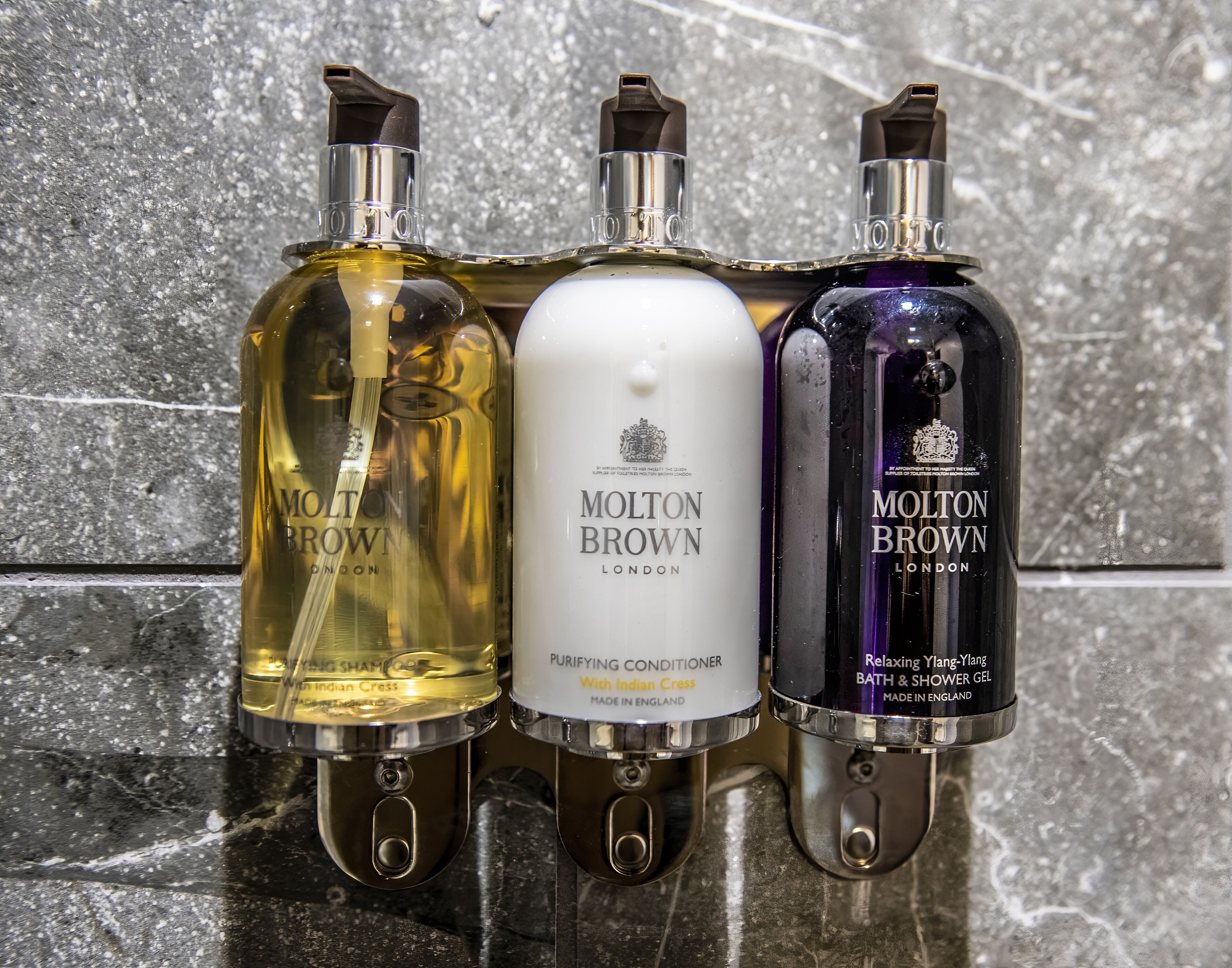 Three bottles of Molton Brown products on a marble surface.