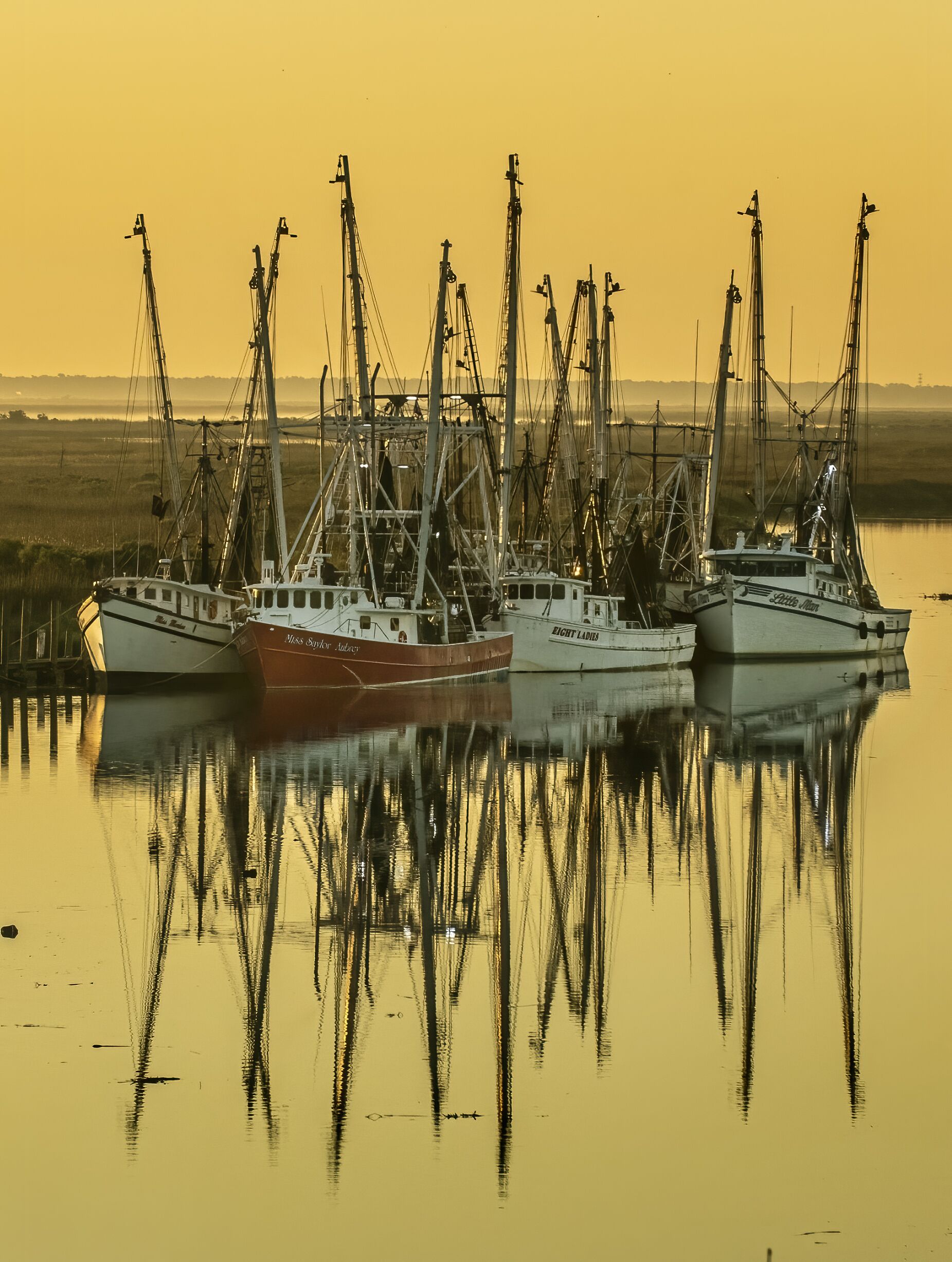 Drie vissersboten liggen aangemeerd in een haven, met rustig water dat hun vormen weerspiegelt.