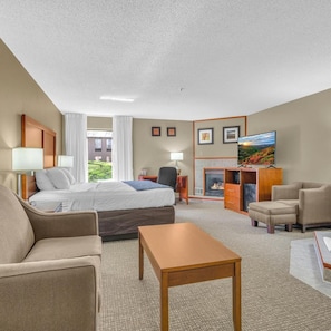 A hotel room with a bed, a sofa, a small table, a TV, a fireplace, and a view of the outdoors. - Bristol Arcadia Inn (Bristol)