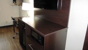 A modern living room with a flat-screen TV mounted on a wooden cabinet, a small table with a lamp, and a compact kitchenette with a microwave. - Red Roof Inn Bristol (Bristol)
