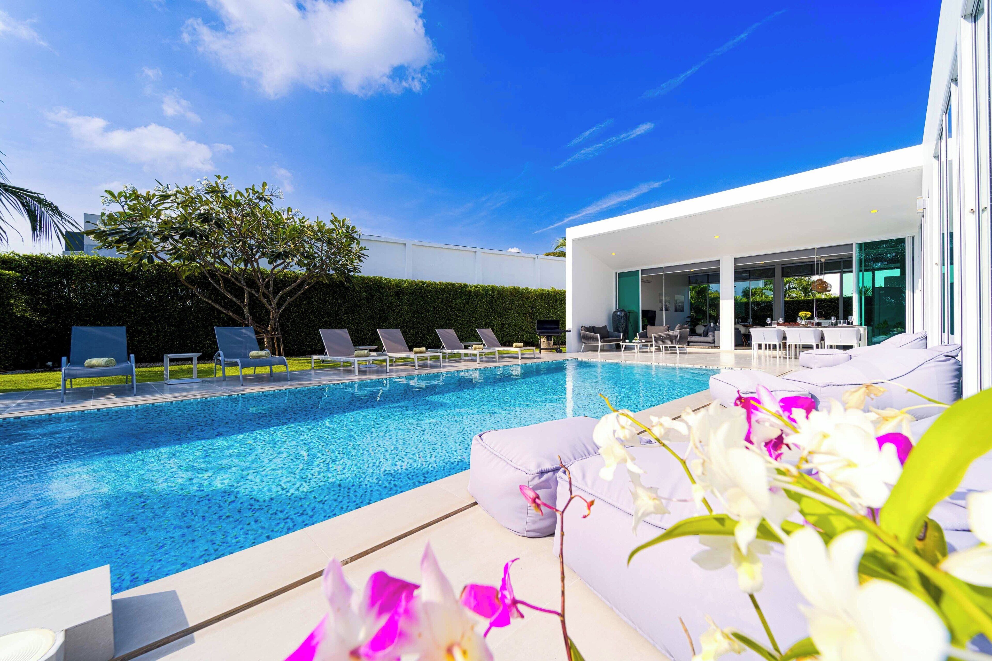 A modern outdoor pool area with lounge chairs and a white building with large windows.