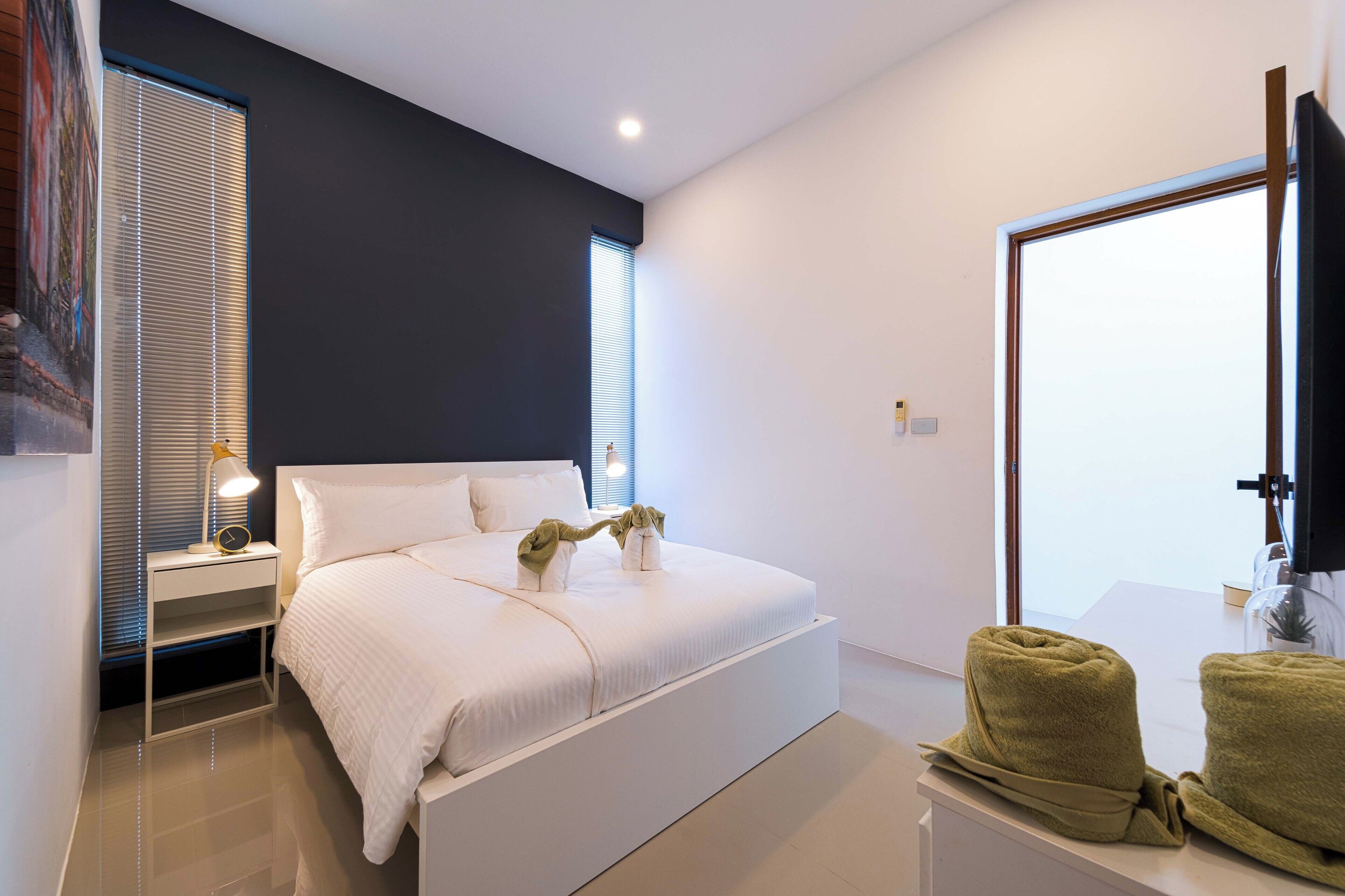 A modern bedroom with a large bed, bedside tables, a nightstand, a flat-screen TV, and a window with blinds.