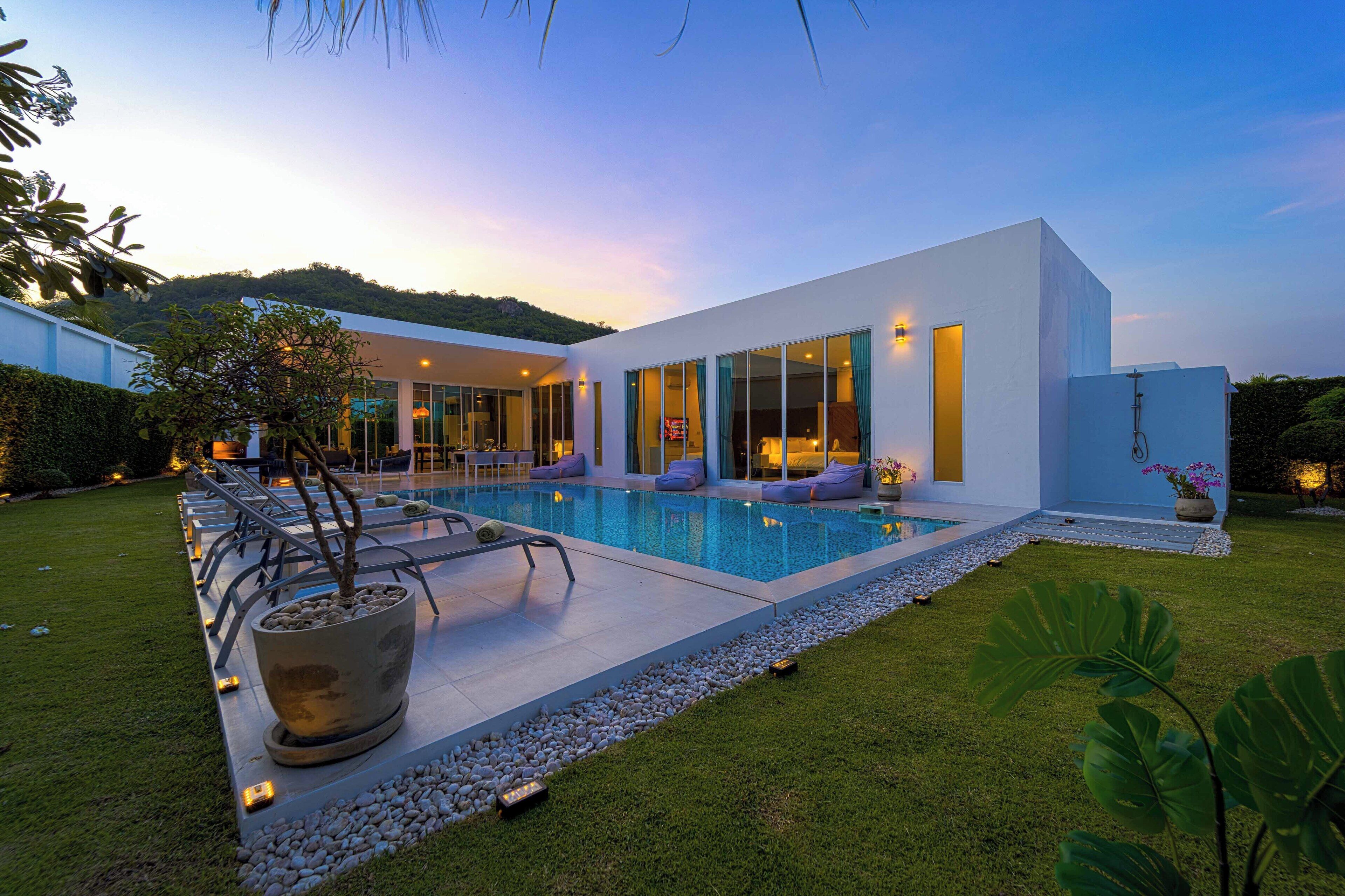 A modern house with a swimming pool, a well-maintained lawn, and a large potted plant.
