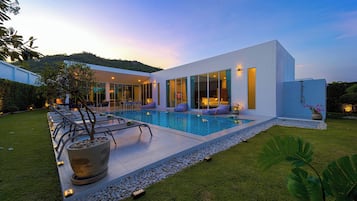 A modern house with a swimming pool, a well-maintained lawn, and a large potted plant.