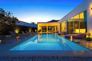 Ein moderner Poolbereich mit Liegestühlen und einem klaren Pool, umgeben von einer gepflegten Hecke und einem zeitgemäßen Gebäude mit großen Fenstern.
