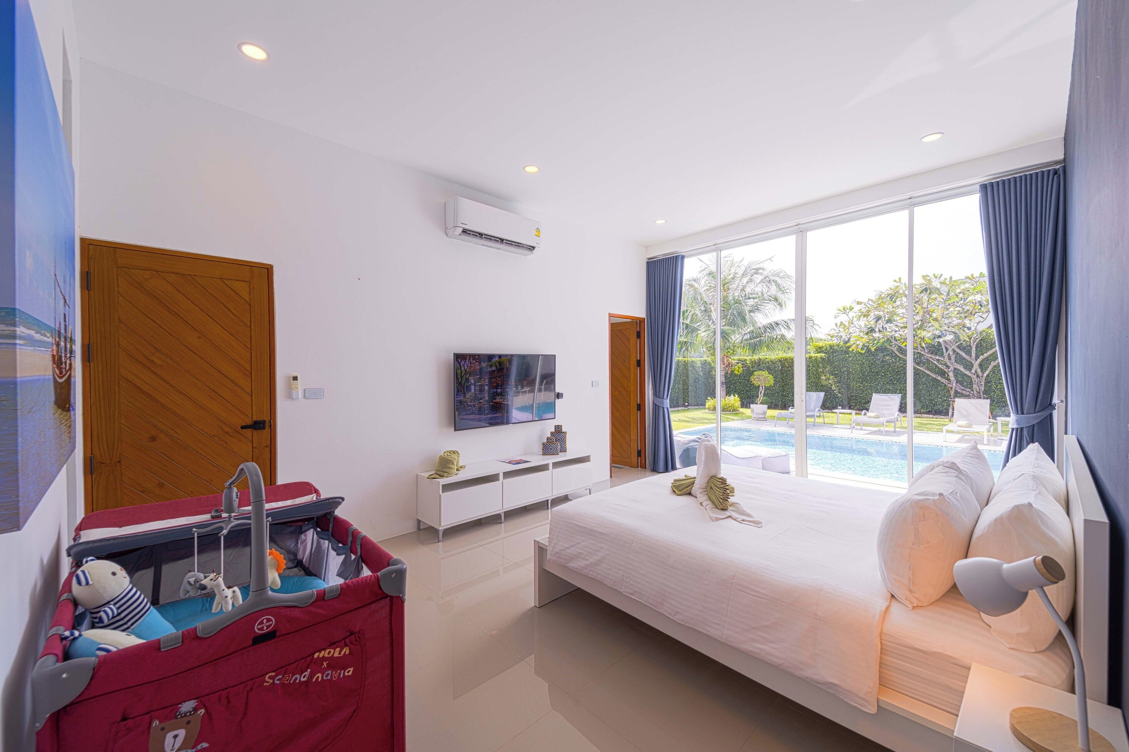 A modern hotel room with a large bed, a TV, a mini fridge, and a view of a swimming pool.