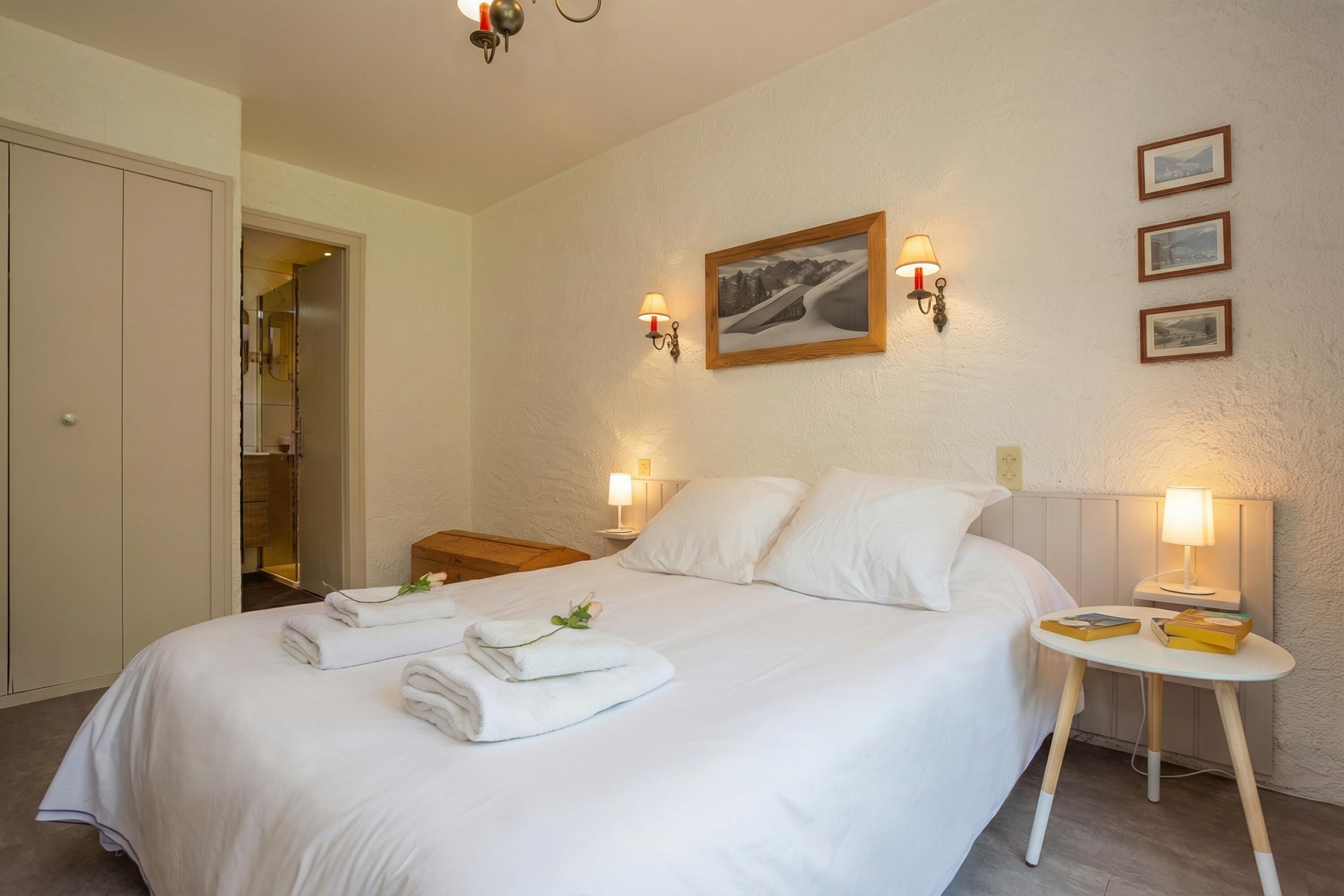 A neatly made bed with towels, a bedside table with books, and wall-mounted lamps.