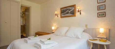 A neatly made bed with towels, a bedside table with books, and wall-mounted lamps.