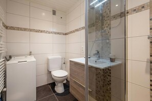 Casa de banho compacta com sanita, máquina de lavar roupa e cabine de duche com parede de vidro.