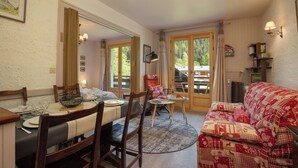 A dining area with a table set for four, chairs, a small round table with a lamp, and a sofa with patterned cushions. - Résidence le Chardonnet G 1BR for 4 w/Shared Pool & panoramic views, Argentière (Chamonix), France (Argentière (Chamonix))