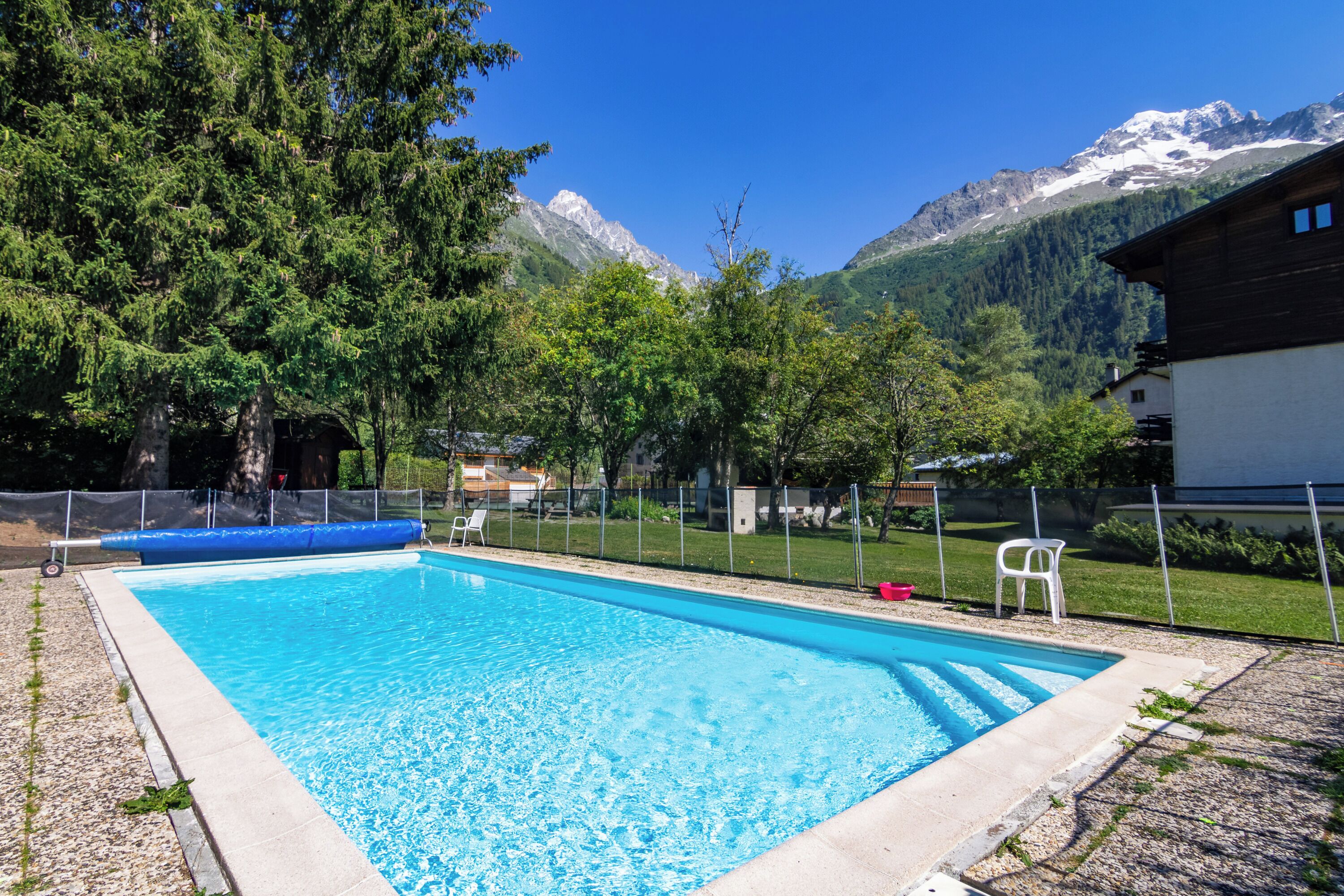 Ein rechteckiger Swimmingpool mit klarem, blauem Wasser, umgeben von einem Zaun, Bäumen und einer Bergkulisse.