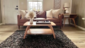 A living room with a brown sofa, a white vase with dried flowers, a wooden coffee table, and a small side table with a lamp. - Cozy cabin retreat in rustic setting. Private lake, bonfire under the stars! (Lake)
