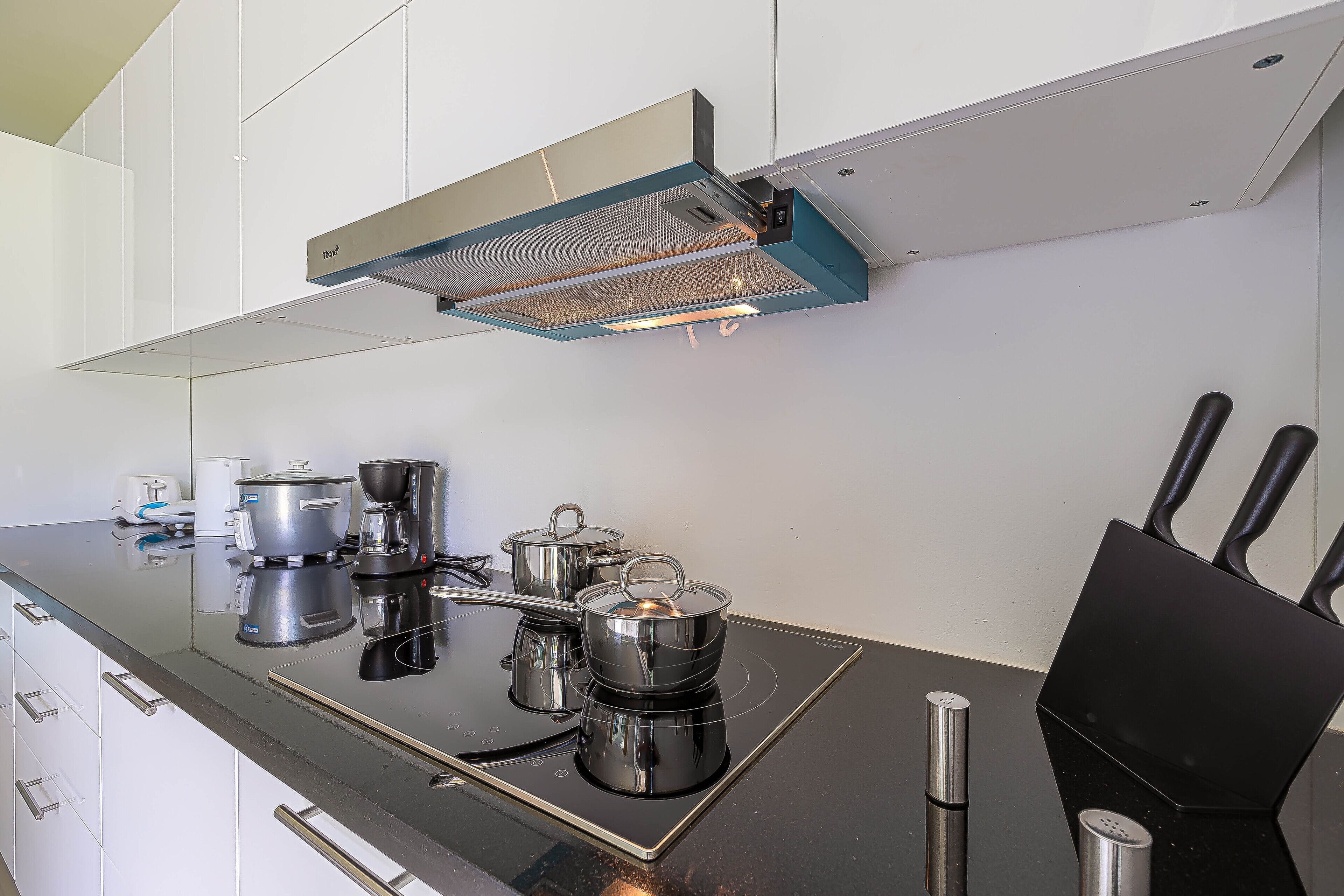 A modern kitchen with a black induction cooktop, stainless steel pots, a coffee maker, and a black knife block.