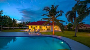 Une piscine avec des chaises longues, une maison avec un toit rouge et des palmiers.