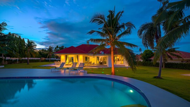 Ein Swimmingpool mit Liegestühlen, ein Haus mit rotem Dach und Palmen.