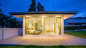 Ein modernes Haus mit einer verglasten Wohnbereitschaft, einem sichtbaren Schlafzimmer mit Bett und einer Terrasse.