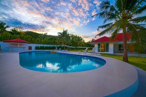 Une piscine avec des chaises longues, un palmier et une maison avec un toit rouge.