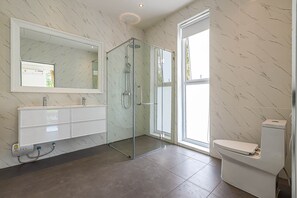 Une salle de bain moderne avec une douche à parois de verre, des toilettes blanches et un meuble-lavabo avec un miroir.