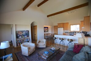 Relax in this inviting living space with a comfortable sofa, coffee table, and bookshelf, adjacent to a fully equipped kitchen.
