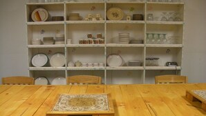 A dining area with a wooden table and chairs, surrounded by shelves with various dishes and glassware. - Panguitch Inn Motel (Panguitch)